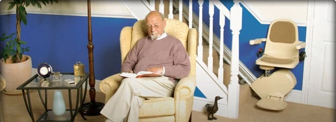 Person relaxing at home with a stairlift fitted to the staircase in the background